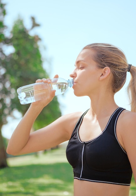 Close-up di una giovane donna che beve acqua contro il cielo
