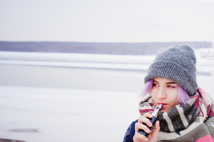 Foto close-up di una giovane donna che fuma in piedi su un campo coperto di neve contro il cielo