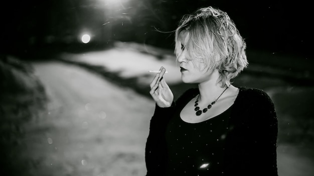 Close-up di una giovane donna che fuma una sigaretta di notte