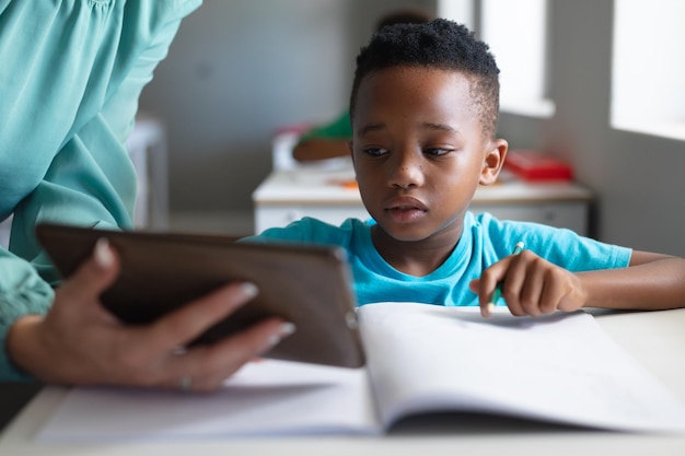 Close-up di una giovane insegnante caucasica che mostra un tablet digitale a un ragazzo di scuola elementare afroamericano