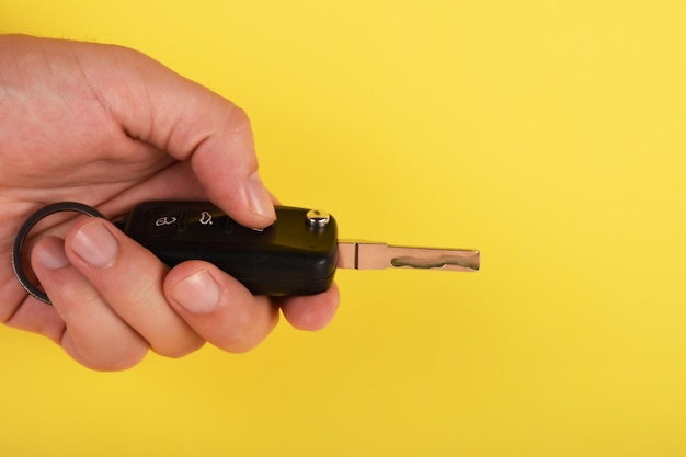 Close-up di una mano che tiene la chiave dell'auto a telecomando sullo sfondo giallo