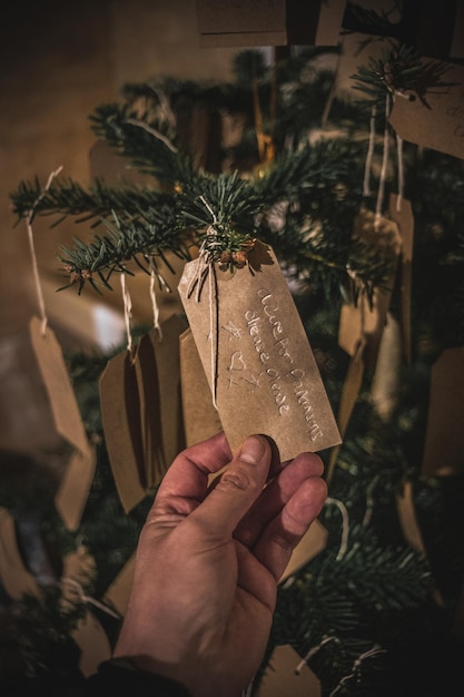 Close-up di una mano che tiene un'etichetta scritta a mano sull'albero dei desideri di Natale