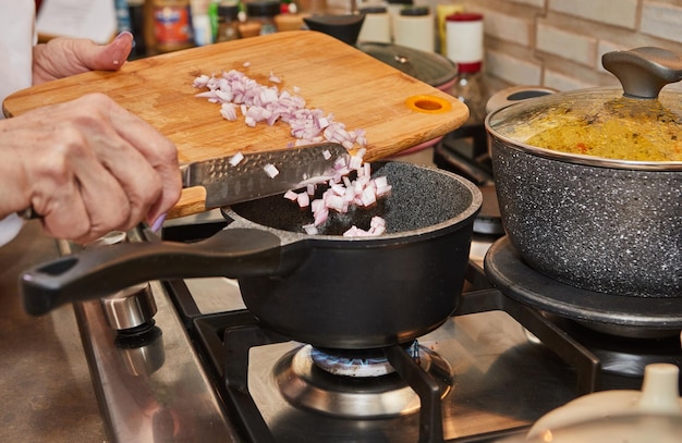 Close-up di una mano di un cuoco che getta scalotti freschi in una padella su una stufa a gas