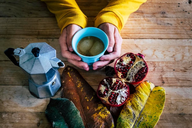 Close up di una persona tagliata che fa colazione a casa con caffè e frutta pomegranato in autunno decorazione foglie colori concetto cibo sano stile di vita tavolo in legno Moka caffè persone irriconoscibili