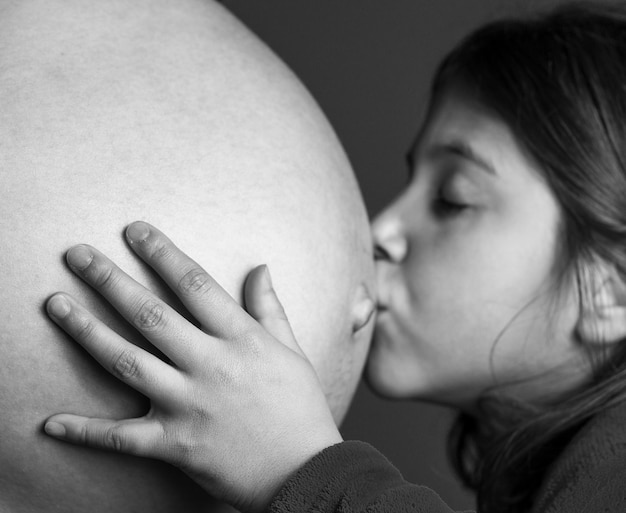 Close-up di una ragazza che bacia l'addome di una madre incinta