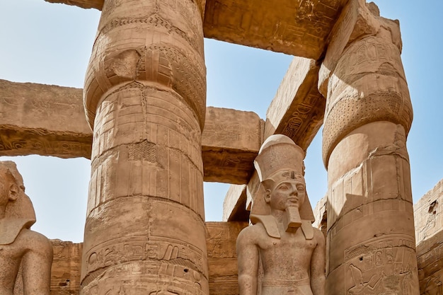 Close-up di una statua di pietra tra colonne che raffigura un faraone egiziano all'interno del tempio di Karnak