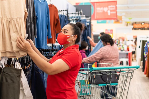 Close-up Donna che indossa una maschera che ha scelto i vestiti per il suo giorno speciale nel reparto abbigliamento femminile di un supermercato in una giornata casuale Concetto per lo shopping stile di vita attenzione selettiva sfocato sullo sfondo