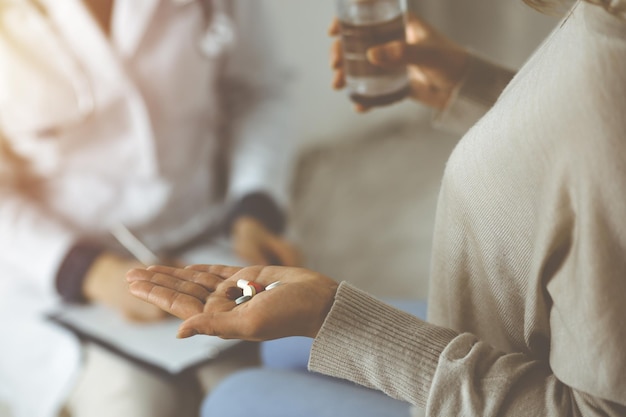 Close-up donna-paziente con le pillole vicino al suo medico, tempo per prendere i farmaci per il mal di testa. Il concetto di stare a casa durante la pandemia di coronavirus e la quarantena di auto-isolamento. Covid 2019.