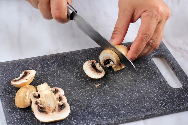 Close up femminile taglio a mano per affettare funghi champignon su marmo nero tagliere