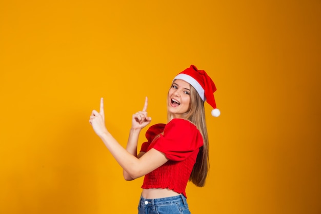 Close up foto positivo ragazza in cappello di babbo natale che punta l'indice, copyspace modo diretto x-mas natale capodanno annunci promozione isolato colore giallo sfondo