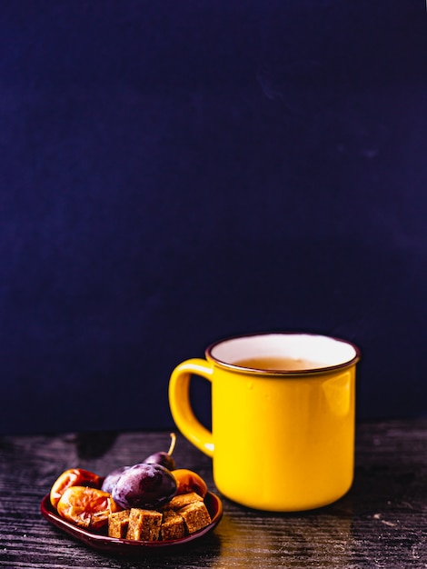 Close up giallo tazza da tè su supporto in legno, sfondo blu scuro, frutta su un piccolo piatto in ceramica