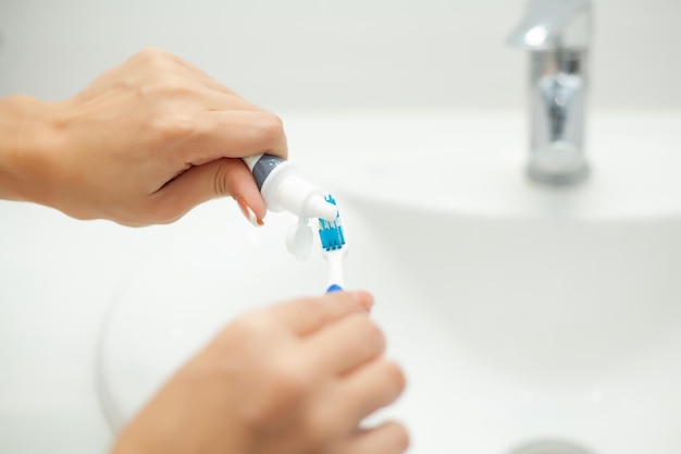 Close up mani donna uso spazzolino da denti in bagno leggero.