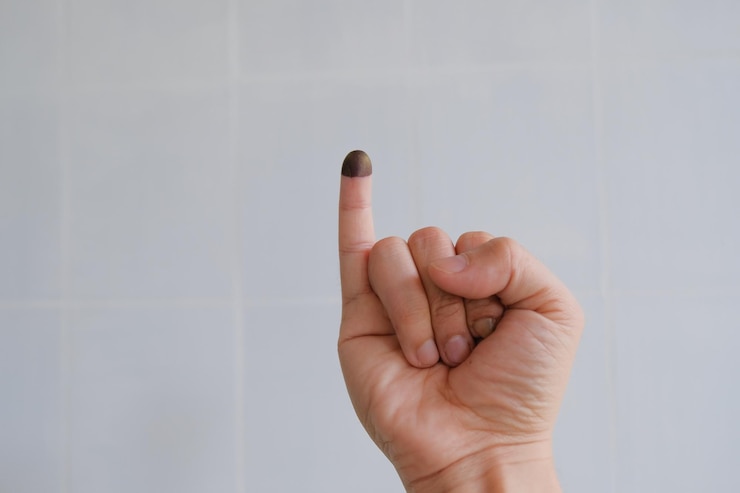 Photo close-up of cropped hand with voting ink against wall
