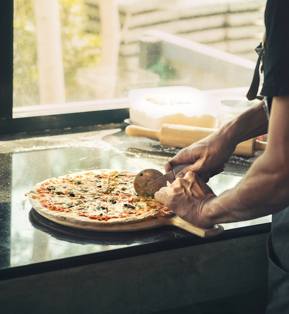 Close up of mano Chef camicia nera taglio di pizza appena sfornato