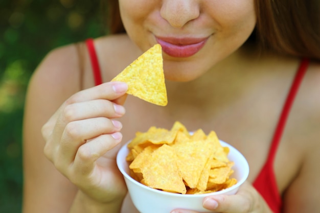 Close up ritratto di donna che mangia tortilla chips con una ciotola piena in mano.