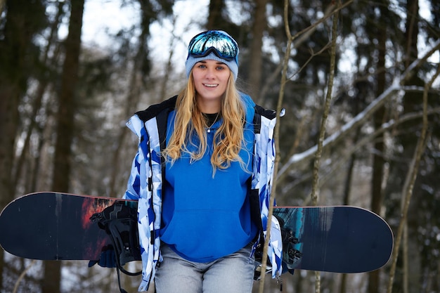 Close up ritratto di donna snowboarder presso la stazione sciistica indossando casco e occhiali con riflesso della foresta in montagna. Spazio di copia gratuito per le tue informazioni.