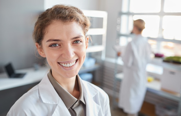Close up ritratto di giovane donna scienziato che guarda l'obbiettivo e sorridente mentre in piedi n laboratorio medico, copia dello spazio