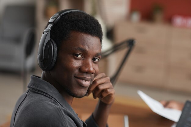 Close up ritratto di giovane musicista afro-americano che indossa le cuffie e sorridere alla telecamera durante la composizione di musica in studio di registrazione a casa, copia dello spazio