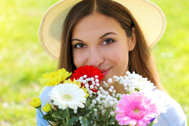 Close up ritratto di ragazza con cappello profumato bouquet di fiori che guarda l'obbiettivo in primavera