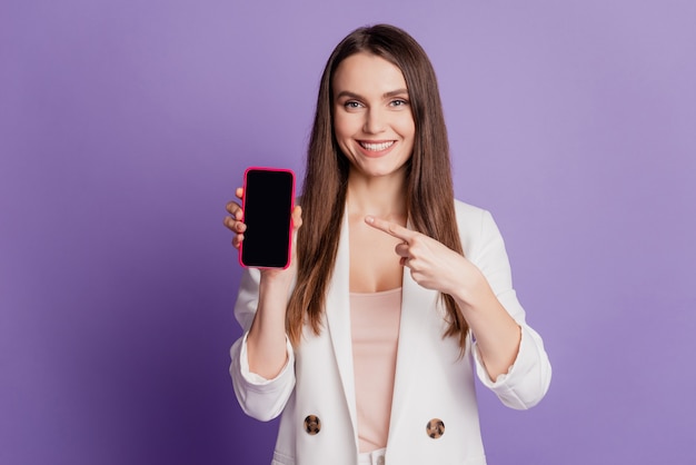 Close up ritratto di signora tenere gadget telefono diretto dito touch screen spazio vuoto indossare abito formale in posa su parete viola