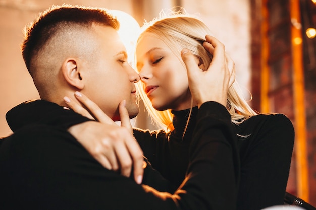 Close up ritratto di un bel giovane uomo e donna mentre l'uomo sta toccando i capelli della sua ragazza prima del bacio contro una luce.