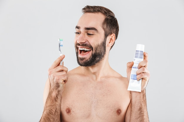 Close up ritratto di un bell'uomo barbuto in piedi isolato su bianco, mostrando dentifricio e spazzolino da denti