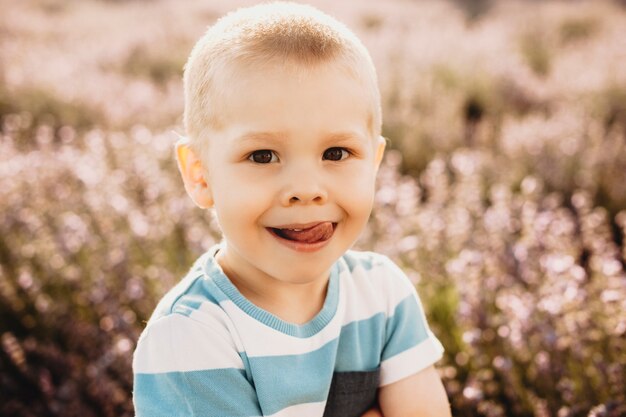 Close up ritratto di un dolce ragazzino divertendosi all'aperto. Piccolo bambino sveglio che guarda l'obbiettivo fuori nel campo dei fiori.