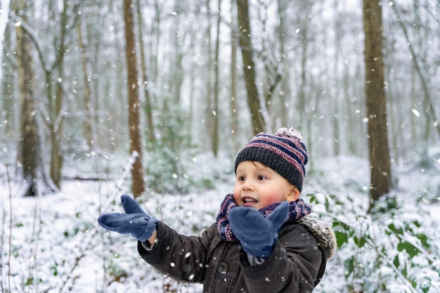 Close up ritratto di un ragazzino che gioca con i fiocchi di neve in un parco in inverno. Il bambino felice gode della prima neve in una foresta. Aspettando il Natale.3