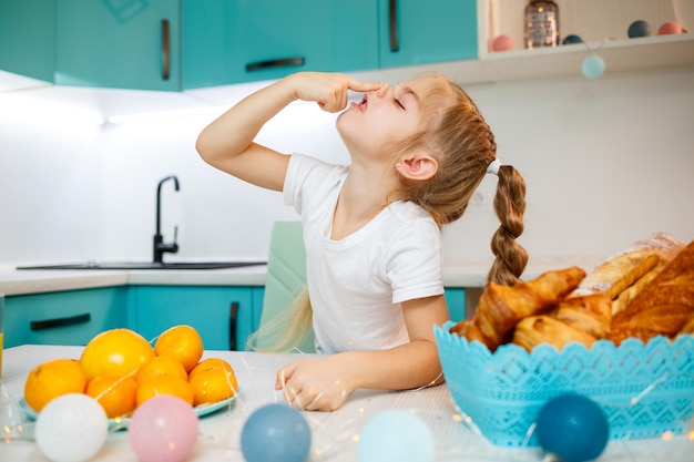 Close up ritratto di una bambina di sette anni. Scherzare seduti al tavolo in cucina. Vestito con una maglietta bianca