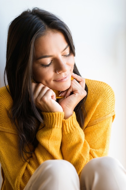 Close up ritratto di una bella giovane donna vestita di maglione seduto alla finestra in interni, gli occhi chiusi