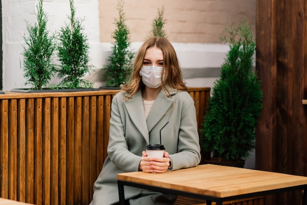 Close up ritratto di una donna caucasica che indossa una maschera medica e in piedi in strada contro un caffè