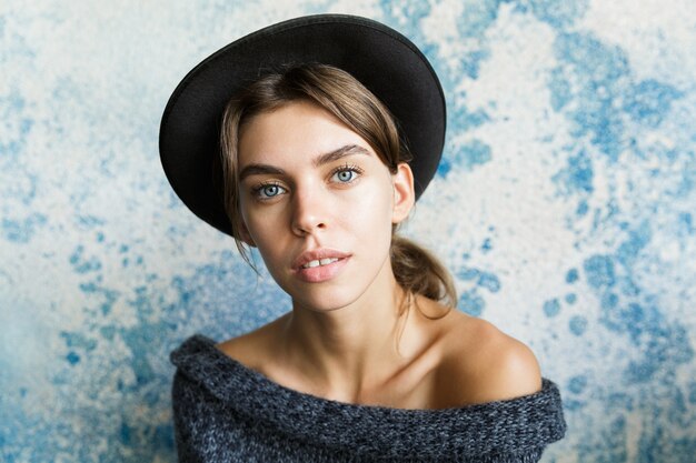 Close up ritratto di una giovane donna vestita di maglione e cappello sul muro blu