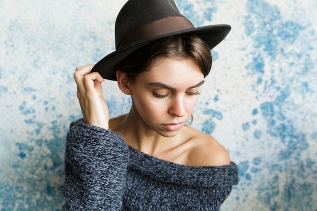 Close up ritratto di una giovane donna vestita in maglione e cappello oltre il muro blu, posa