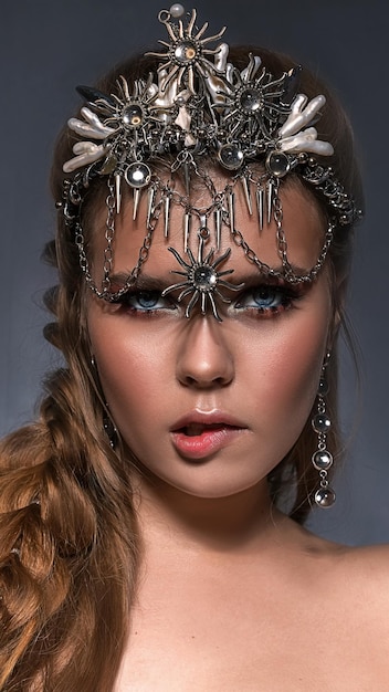 Close up ritratto di una giovane e bella donna bionda che indossa una corona e bigiotteria su un ba grigio