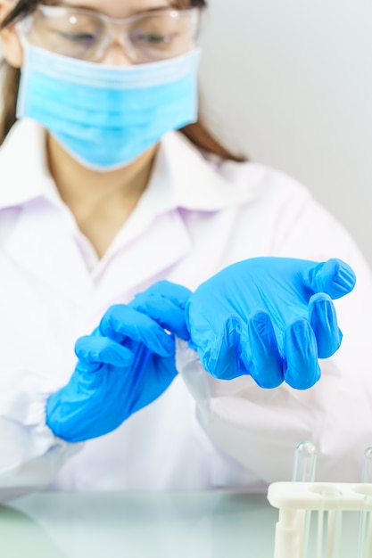 Close up Scienziato mani mettendo in nitrile guanti di lattice blu in camice da laboratorio indossando guanti di nitrile, facendo esperimenti in laboratorio