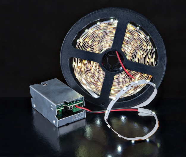 Close-up Shining LED Light Strip sulla bobina e adattatore di tensione, sul nero.