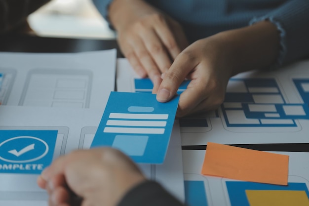 Close up ux developer and ui designer brainstorming about mobile app interface wireframe design on table with customer breif and color code at modern officeCreative digital development agency