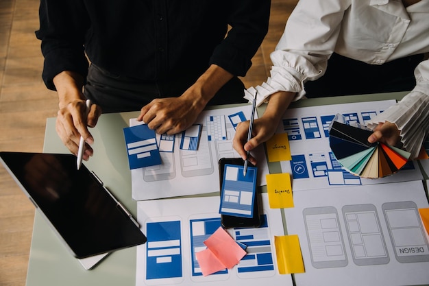 close up ux developer and ui designer brainstorming about mobile app interface wireframe design on table with customer breif and color code at modern officecreative digital development agency