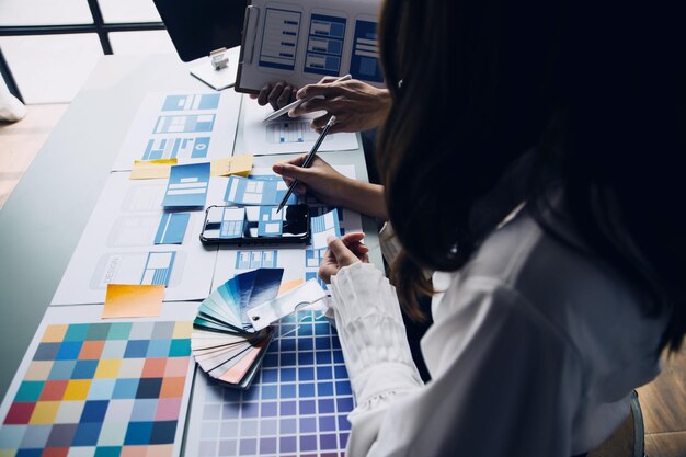 Close up ux developer and ui designer brainstorming about mobile app interface wireframe design on table with customer breif and color code at modern officeCreative digital development agency
