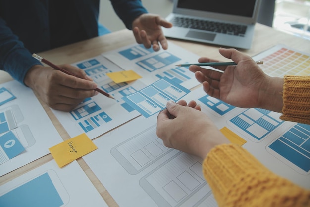 close up ux developer and ui designer brainstorming about mobile app interface wireframe design on table with customer breif and color code at modern officecreative digital development agency