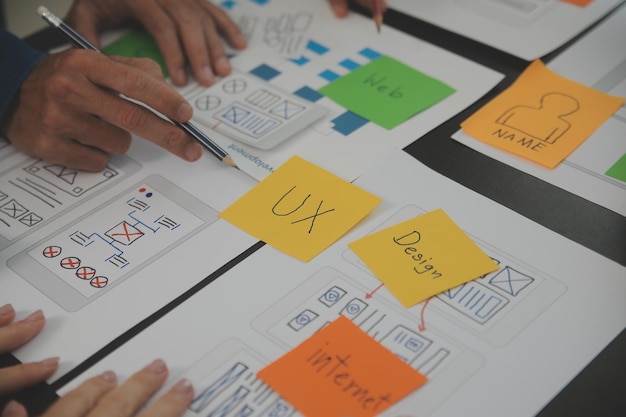 Close up ux developer e ui designer brainstorming sulla progettazione wireframe dell'interfaccia dell'app mobile sul tavolo con breif del cliente e codice colore presso l'ufficio modernoAgenzia di sviluppo digitale creativo