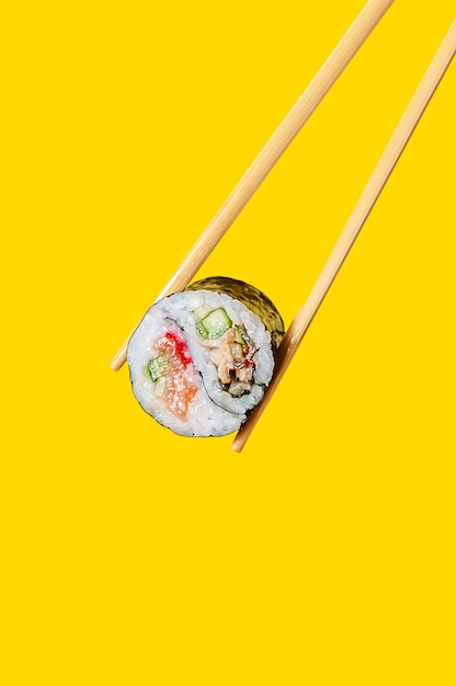 Close up Yin-Yang Roll con salmone, anguilla e cetriolo su bacchette su sfondo giallo.