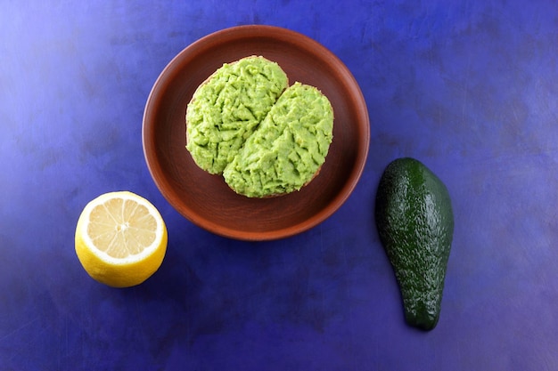 Closeup colazione vegetariana toast con avocado smash su un piatto di argilla Toast e avocado verde e limone giallo su sfondo blu Vista dall'alto