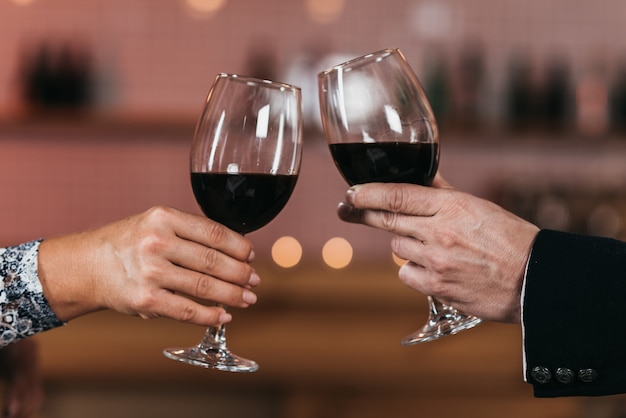 Closeup di bicchieri con vino rosso nelle mani di un uomo e una donna al centro del telaio