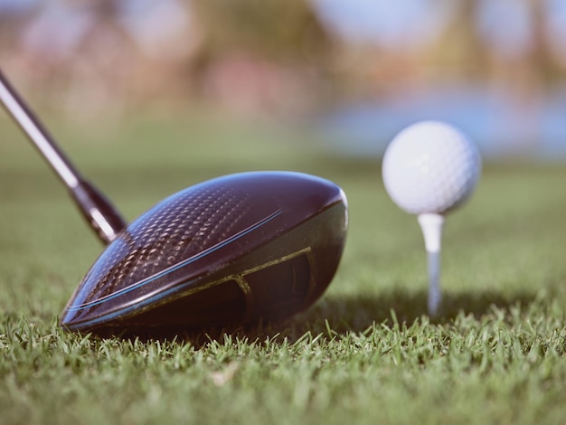 Closeup di un club di golf nero vicino a una palla da golf bianca su un piccolo stand posizionato sul prato verde del campo da golf alla luce del sole