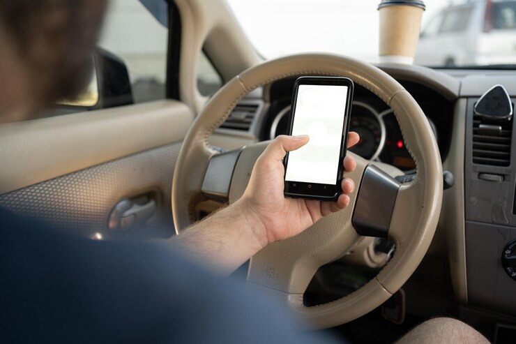 Foto closeup di un uomo che tiene in mano uno smartphone con un mockup bianco sullo sfondo dello schermo del volante dell'auto che cerca la posizione tramite l'applicazione gps navigatore