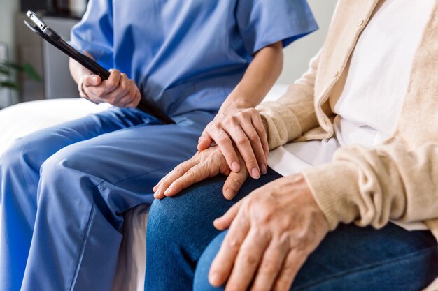 Closeup di una donna asiatica anziana con la mano del suo caregiver che aiuta le mani del caregiver in visita a casa