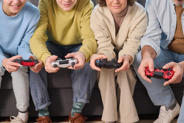 Closeup di una famiglia di quattro persone che usano i joystick per giocare insieme a casa