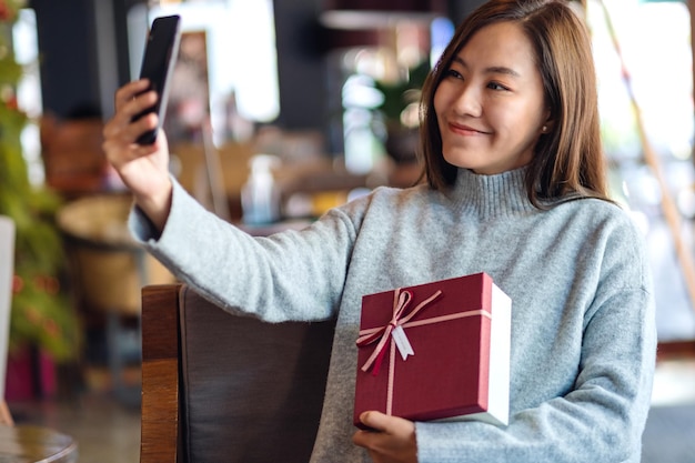 Closeup image of a beautiful young asian woman using mobile phone to take selfie with gift box