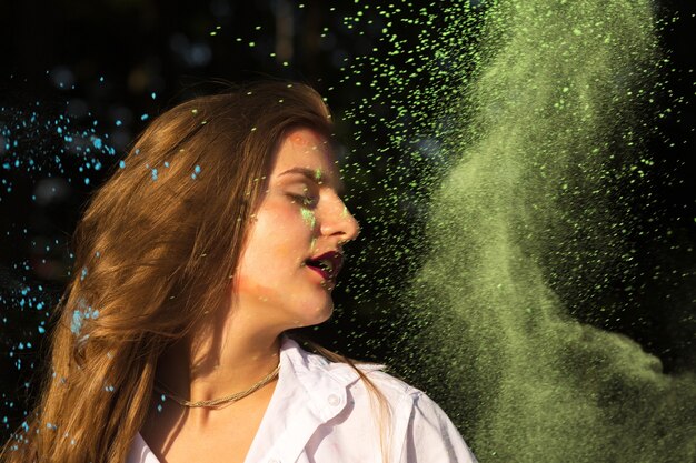 Closeup ritratto di bella donna bionda con i capelli lunghi in posa con vernice Holi che esplode intorno a lei